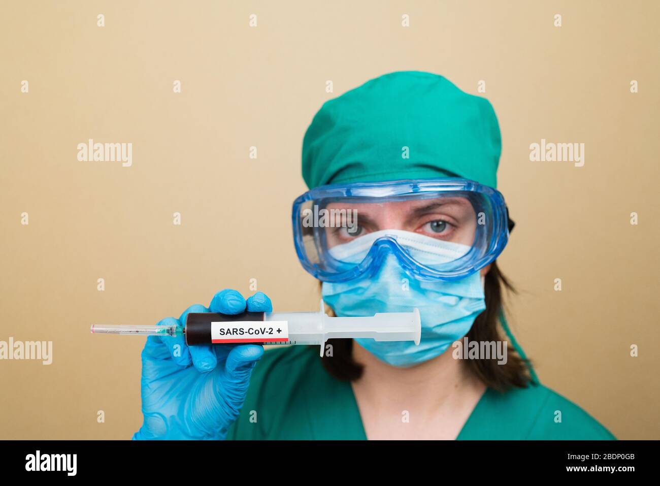 Le médecin féminin en costume vert et les gants bleus contiennent une seringue avec du sang positif COVID-19 sur le fond jaune. Concept médical. Mise au point sélective. Banque D'Images