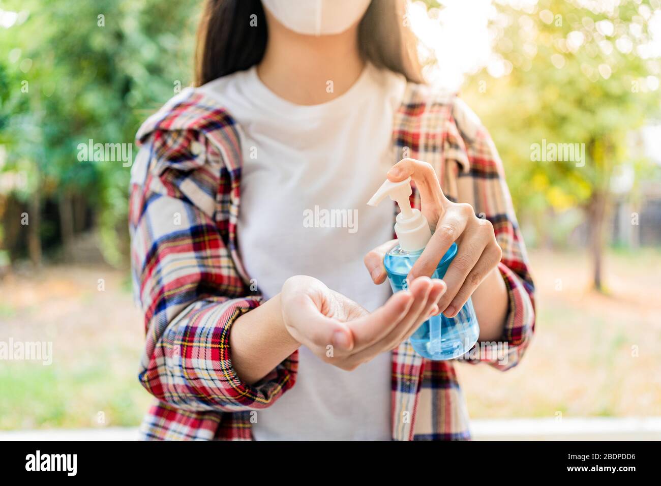 Jeune femme utilisant du gel anti-septique pour la main d'alcool pour nettoyer ses mains, arbres flous et arrière-plan de jardin, bon concept d'hygiène Banque D'Images