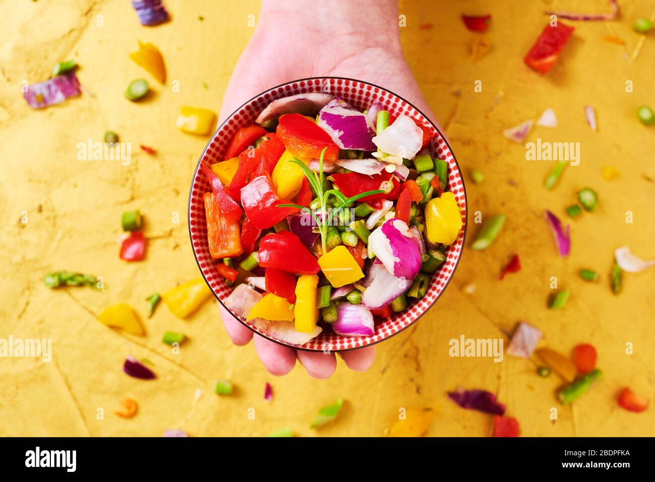 vue en grand angle d'un bol avec un mélange de différents légumes crus hachés, tels que l'asperge, l'oignon ou le poivron jaune et rouge, à la main d'une ma Banque D'Images