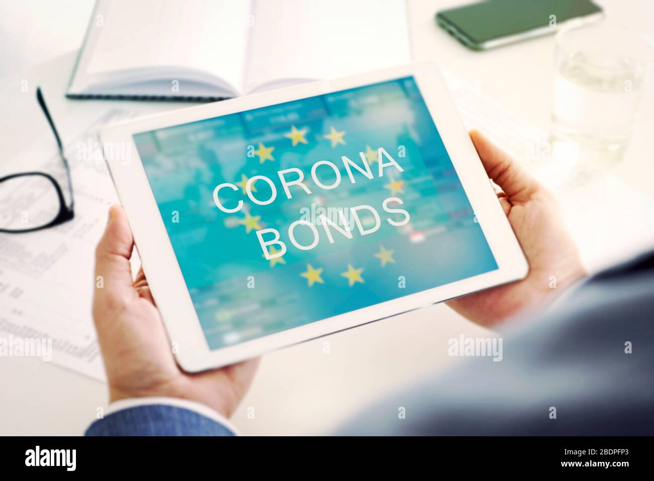 gros plan d'un homme, portant une veste de costume, ayant une tablette numérique dans ses mains avec le texte corona liens dans son écran, assis à un bureau blanc à côté de t Banque D'Images