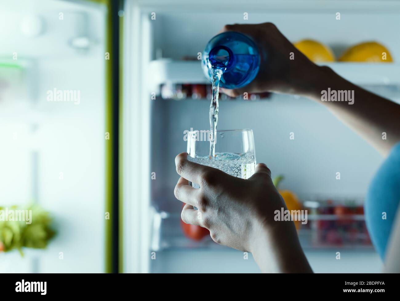 Femme prenant une bouteille d'eau du réfrigérateur et la verser dans un verre Banque D'Images