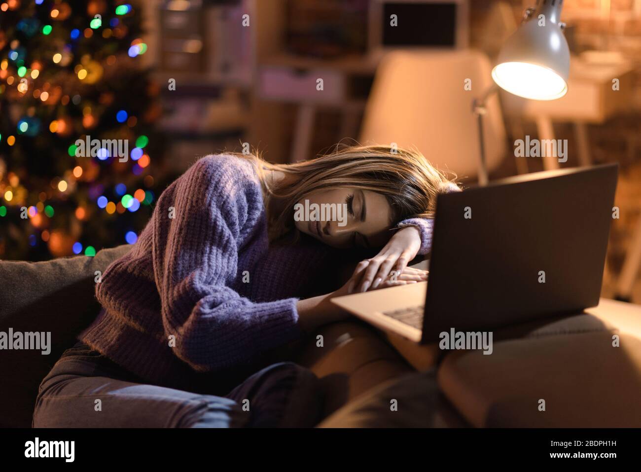 Yound femme dormant sur le canapé à la maison la veille de Noël et arbre de Noël en arrière-plan Banque D'Images