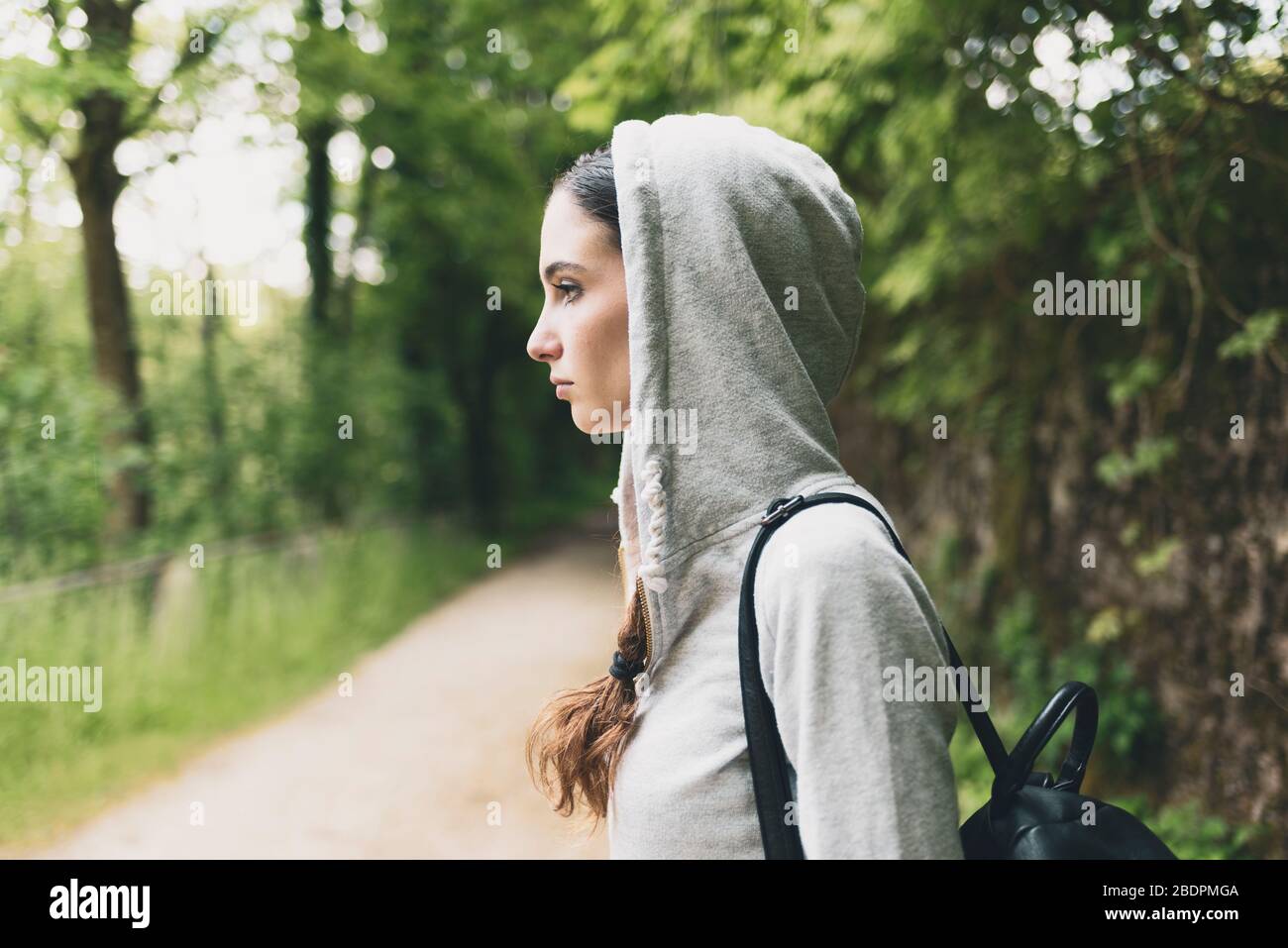 Triste pensive jeune femme avec hoodie marchant dans les bois, elle regarde loin et pense Banque D'Images