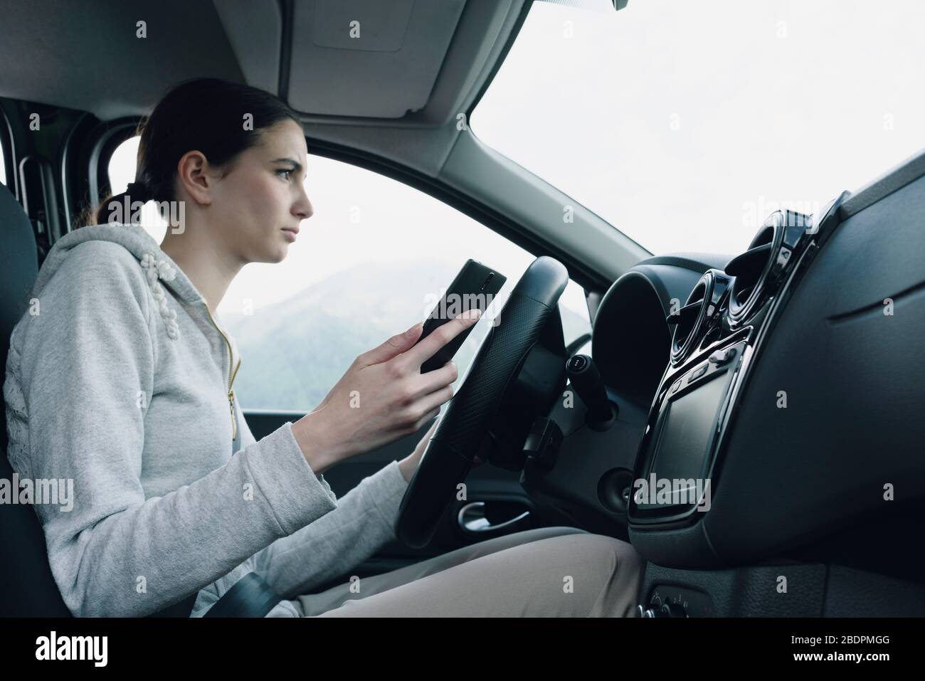 La jeune femme méprise et négligente utilise son smartphone pendant la conduite, en conduisant le concept de sécurité Banque D'Images
