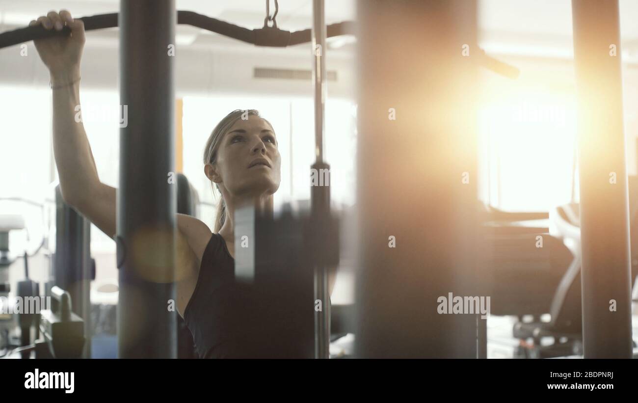 Femme de sport qui fait de l'exercice à la salle de sport, elle travaille avec une machine de pulldown lat Banque D'Images