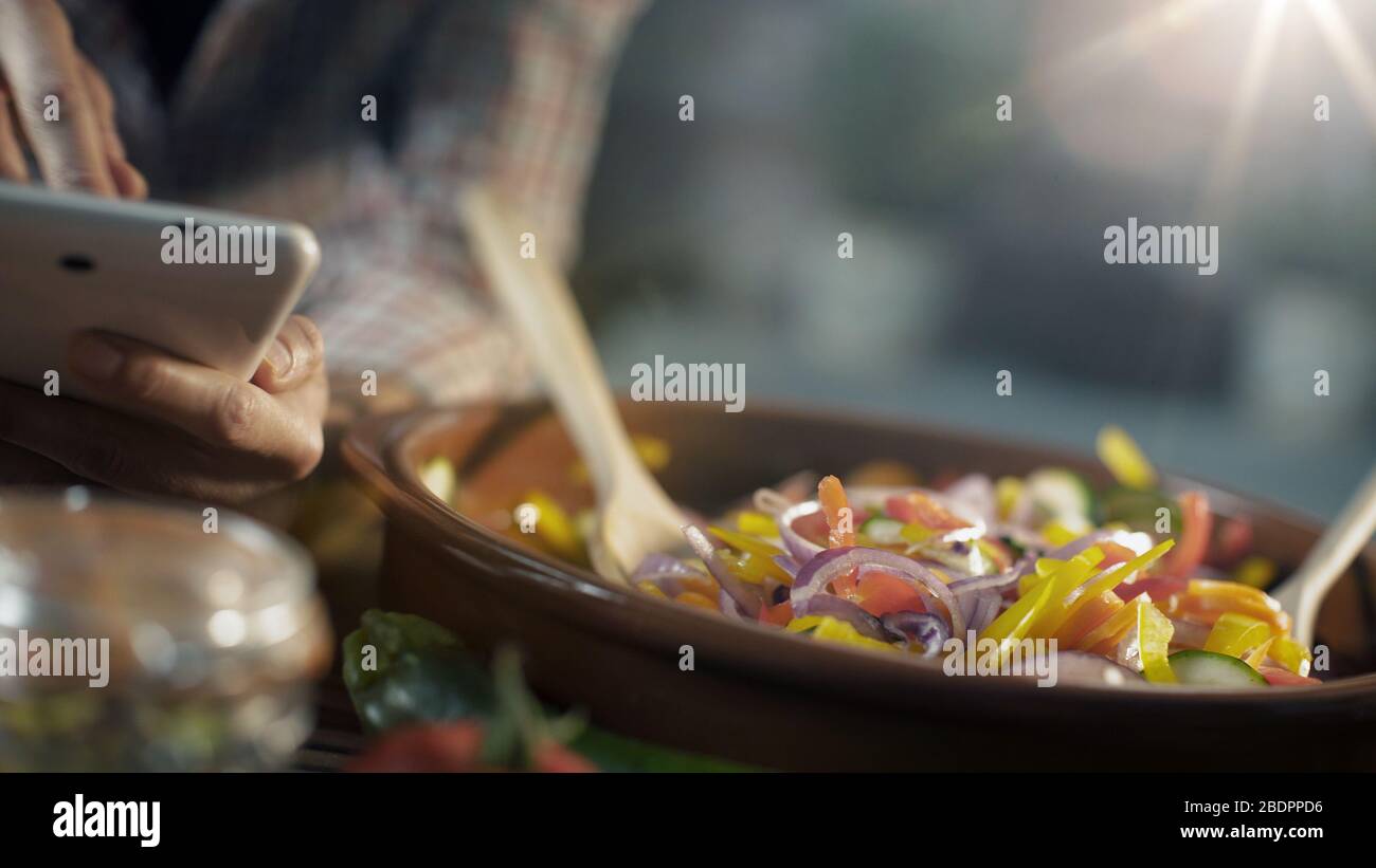 Femme recherchant des recettes saines en ligne sur sa tablette numérique et la cuisine de légumes frais mélangés dans une casserole d'argile Banque D'Images