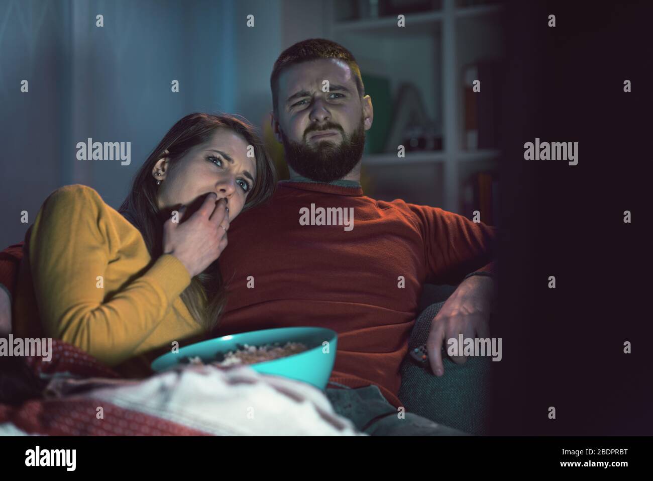 Jeune couple assis sur le canapé à la maison et regarder des films d'horreur ensemble à la télévision, il embrasse sa petite amie Banque D'Images