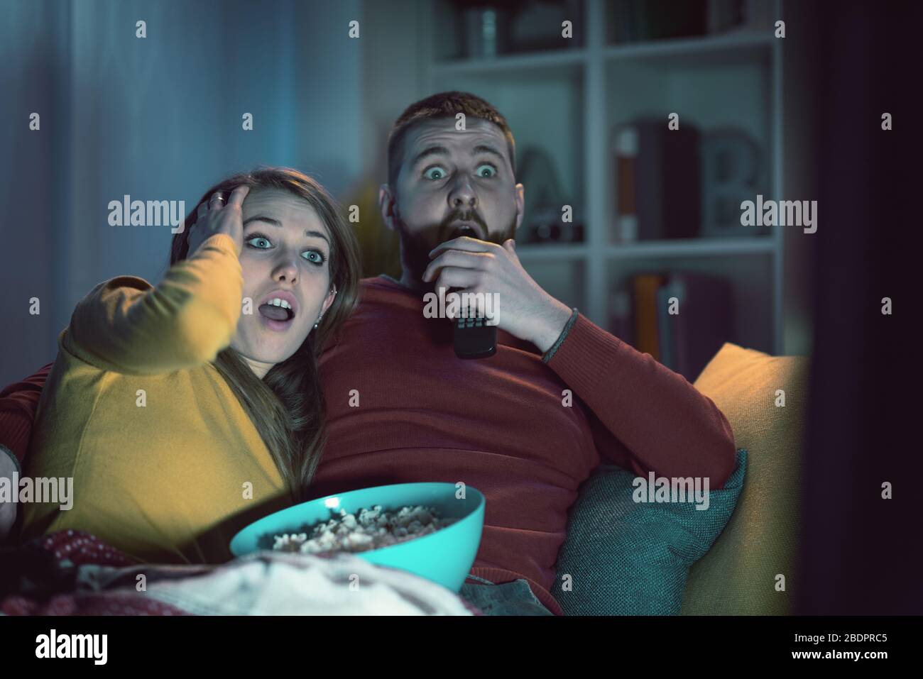 Jeune couple assis sur le canapé à la maison et regarder des films d'horreur ensemble à la télévision, il embrasse sa petite amie Banque D'Images