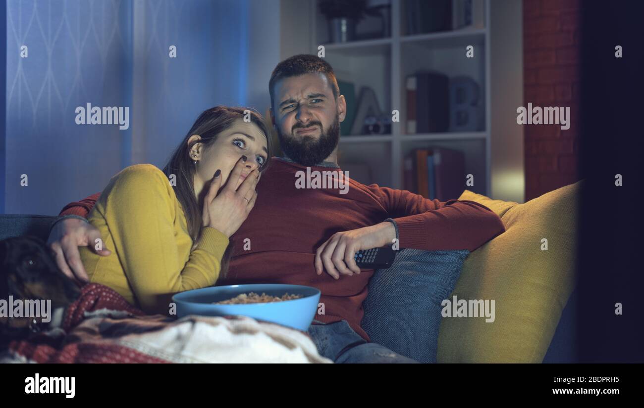 Jeune couple assis sur le canapé à la maison et regarder des films d'horreur ensemble à la télévision, il embrasse sa petite amie Banque D'Images