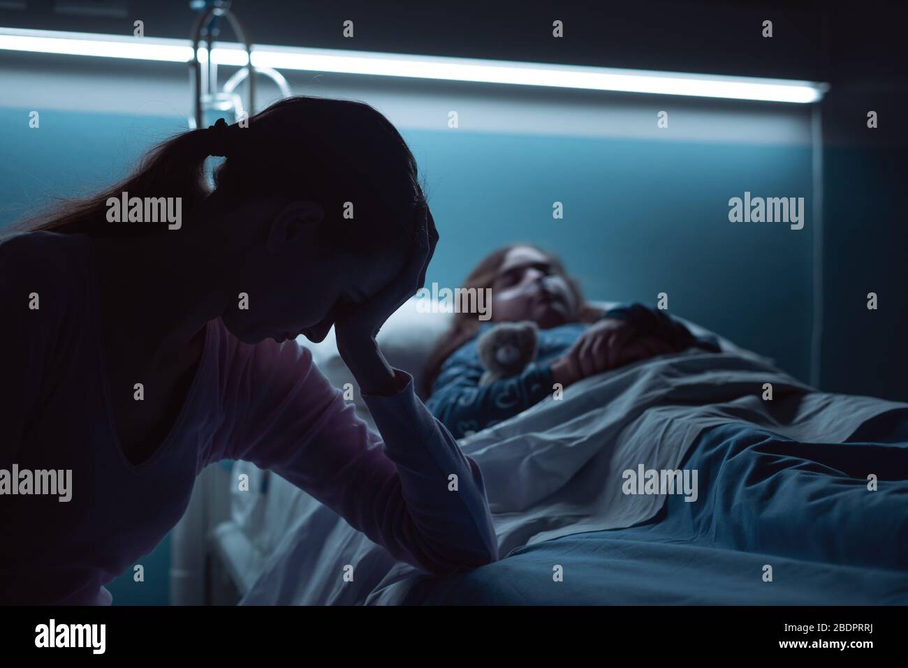 Jeune mère désespérée aidant son enfant malade allongé dans un lit d'hôpital la nuit Banque D'Images