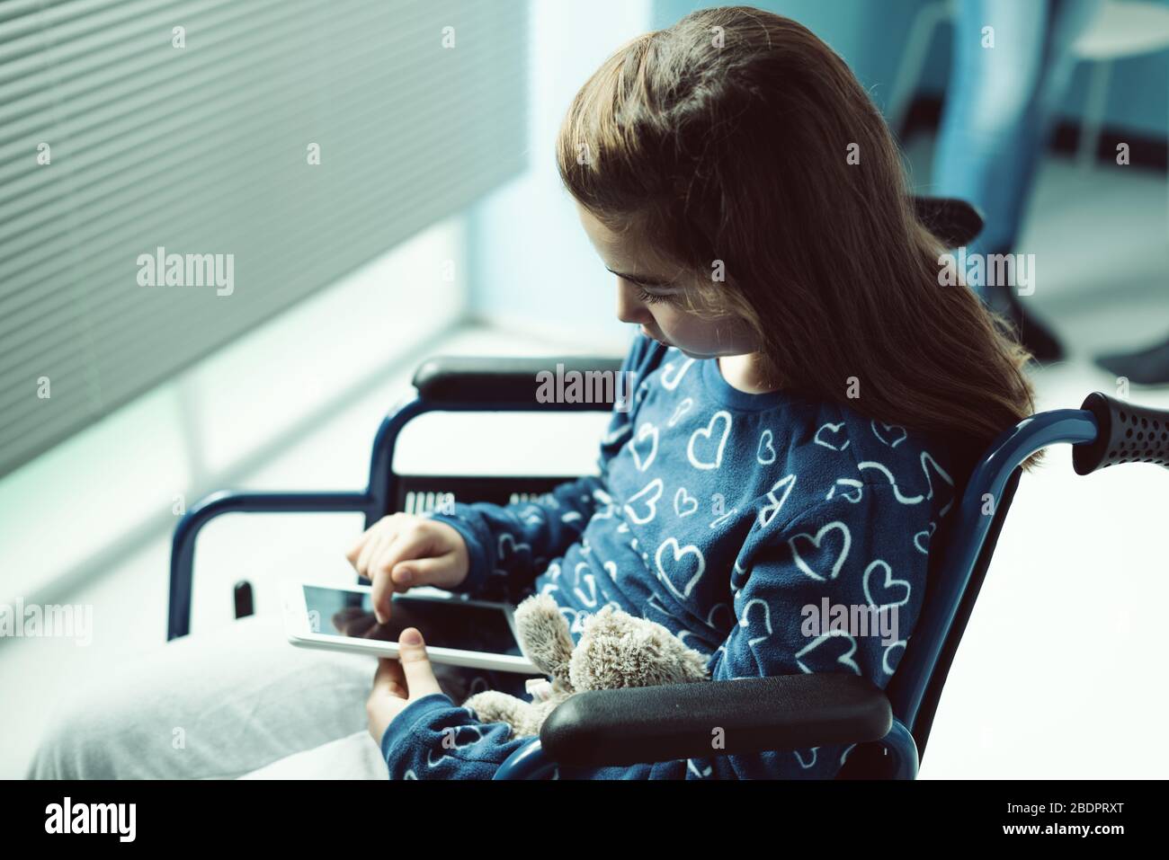 Fille en fauteuil roulant à l'hôpital, elle utilise une tablette numérique Banque D'Images