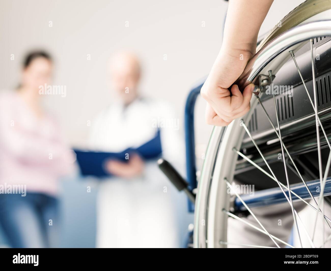 Patient en fauteuil roulant à l'hôpital, une femme et le médecin discutent en arrière-plan, main sur la roue de gros plan Banque D'Images