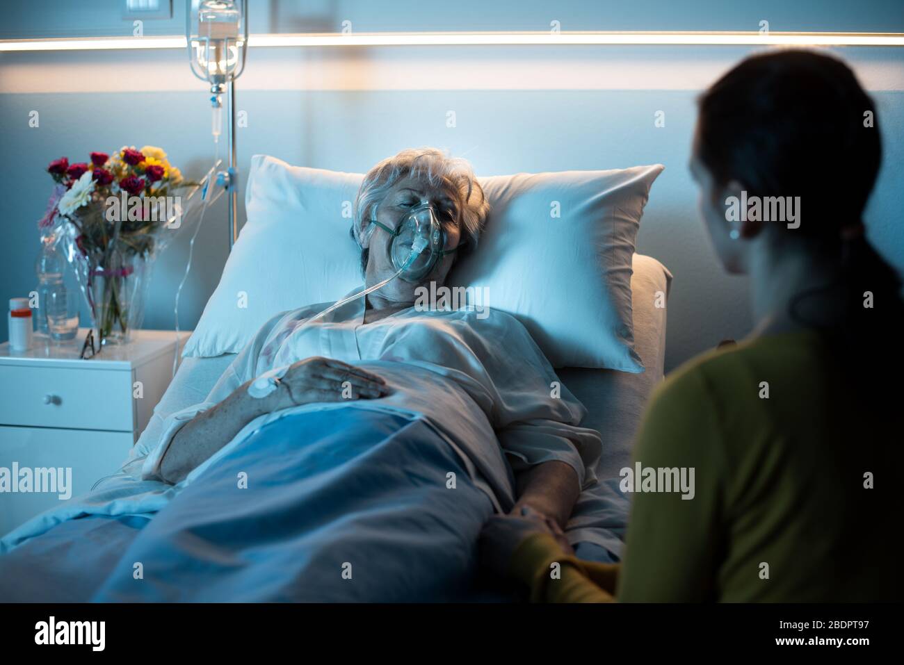 Femme aidant et soutenant sa mère âgée posée dans le lit à l'hôpital, elle tient sa main Banque D'Images