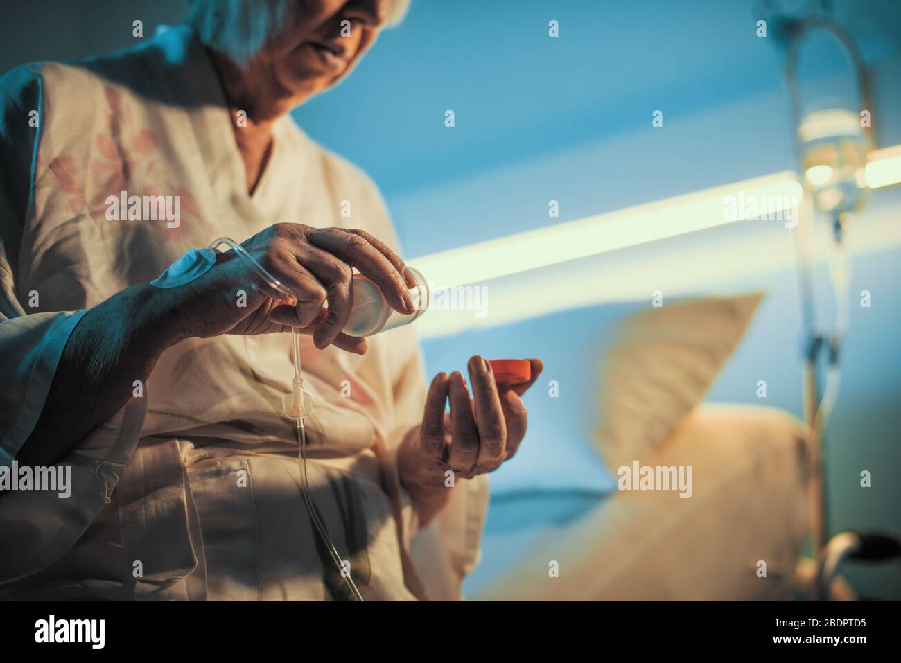 Femme âgée assise sur un lit d'hôpital et prenant des médicaments d'ordonnance Banque D'Images