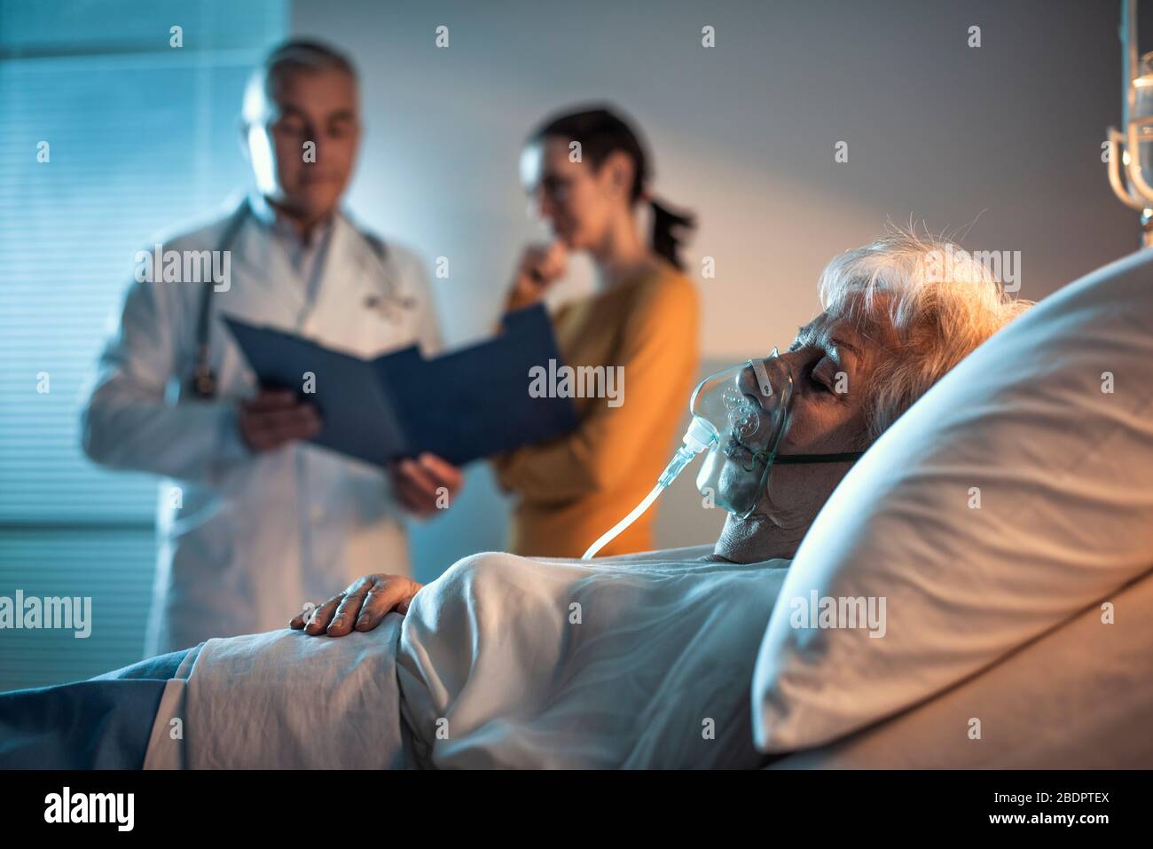 Patient senior à l'hôpital allongé dans le lit et médecin parlant avec un membre de la famille en arrière-plan Banque D'Images