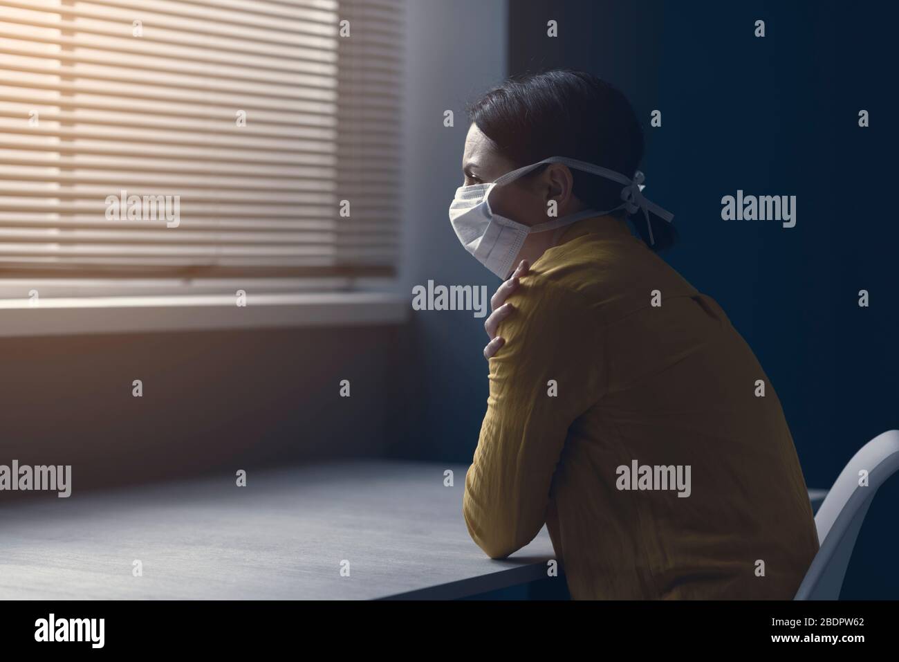 Femme solitaire en quarantaine avec covid-19 portant un masque de visage et assis à la maison seule devant une fenêtre, concept d'urgence d'épidémie de virus Banque D'Images