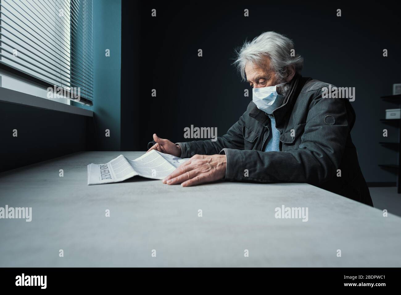 Mis en quarantaine des personnes âgées assis seul à la maison et lisant des informations effrayantes sur le journal concernant le covid-19, il porte un masque chirurgical Banque D'Images