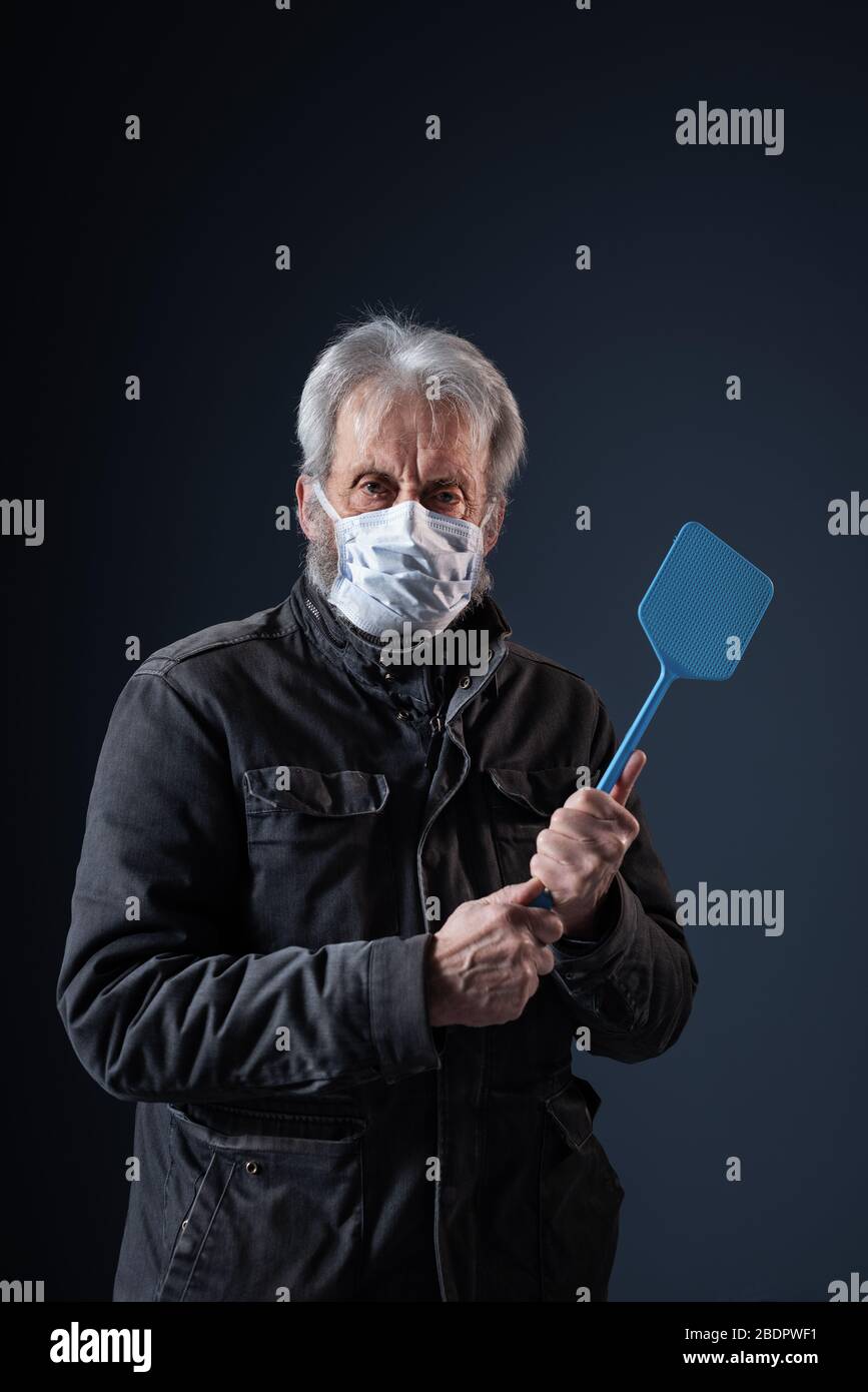 Confiant senior se protégeant contre le virus Covid-19, il porte un masque de visage et tient un swatter Banque D'Images