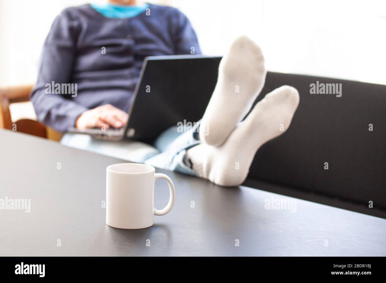 Femme assise dans un canapé avec un ordinateur portable, elle se repose sur une table où une tasse ou une tasse est placée. Foyer sélectif et femme floue. Travail de fréon Banque D'Images