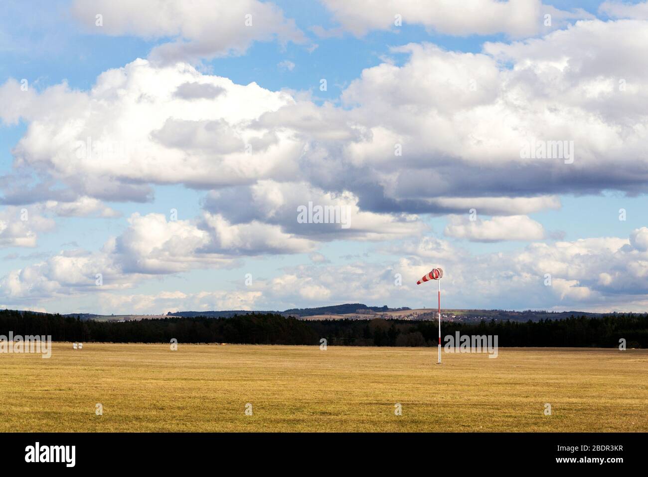 Des chaussettes ventrales rouges et blanches sur un aérodrome herbacé vide, des nuages spectaculaires en arrière-plan, des prévisions météorologiques venteuses et un concept de circulation aérienne Banque D'Images