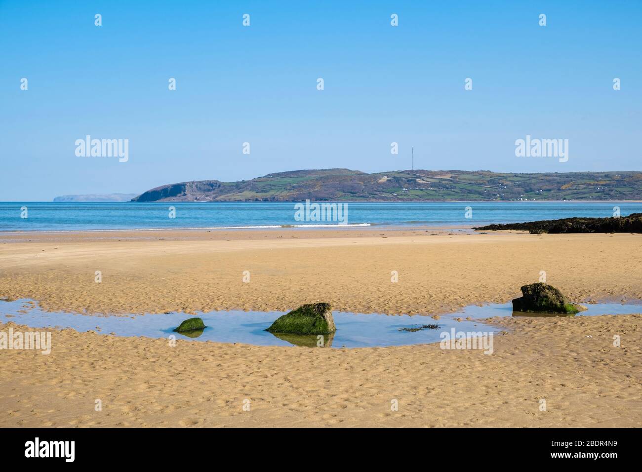 Une piscine à marée sur une belle plage de sable calme avec vue sur Llanddona de l'autre côté de la baie de Red Wharf. Benllech, Île d'Anglesey, Pays de Galles du Nord, Royaume-Uni, Grande-Bretagne Banque D'Images