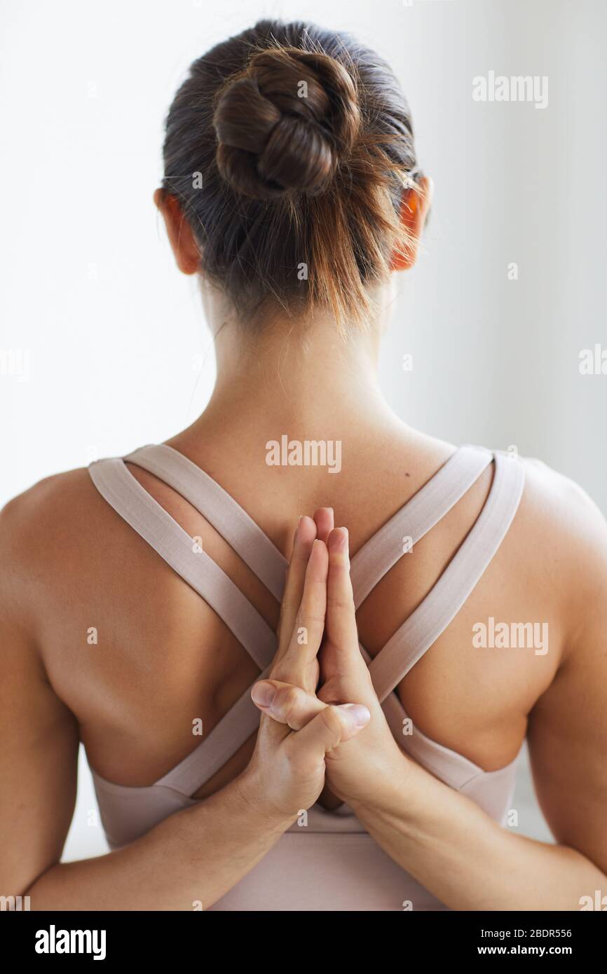 Vue arrière de la jeune femme flexible qui s'étire les mains derrière le dos pendant l'entraînement de yoga Banque D'Images