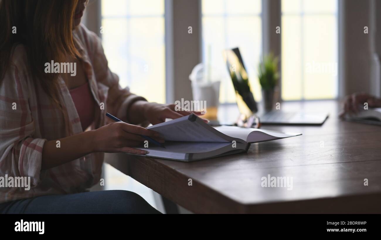 Pantacourt taille haute de belle femme lisant un livre d'école tout en  assis à la table en bois moderne avec des fenêtres de salon comme  arrière-plan Photo Stock - Alamy