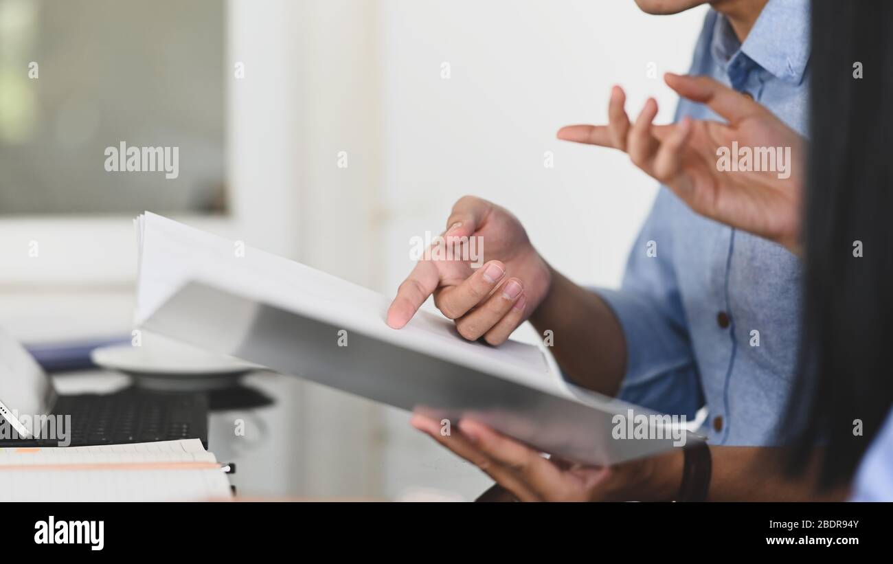Image rognée de l'équipe de développement commercial discutant/réunion sur le résultat de son bénéfice commercial tout en tenant un fichier de document et en étant assis en mode Banque D'Images