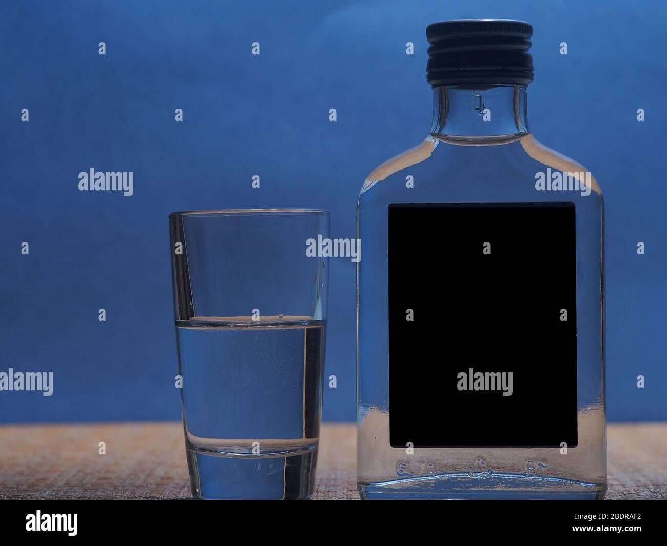 Silhouette d'une petite bouteille de verre avec vodka et d'une pile de verre sur un fond bleu. La vie-fixe. Banque D'Images