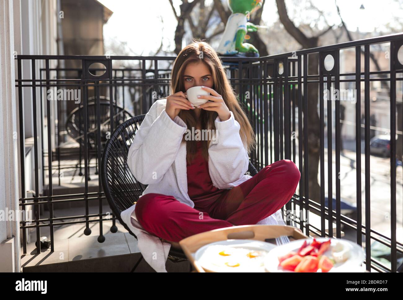 Une gentille dame assise sur le balcon le matin et buvant du thé chaud aromatique. Port d'un peignoir blanc et d'une pyjama bordeaux. Petit déjeuner délicieux Banque D'Images