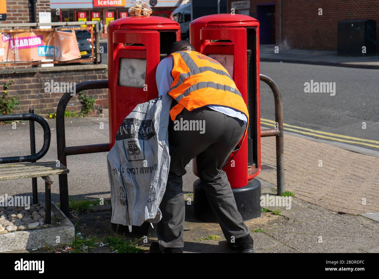 Un postman Royal Mail transportant un sac de courrier qui collecte le courrier d'une boîte postale dans une rue Banque D'Images
