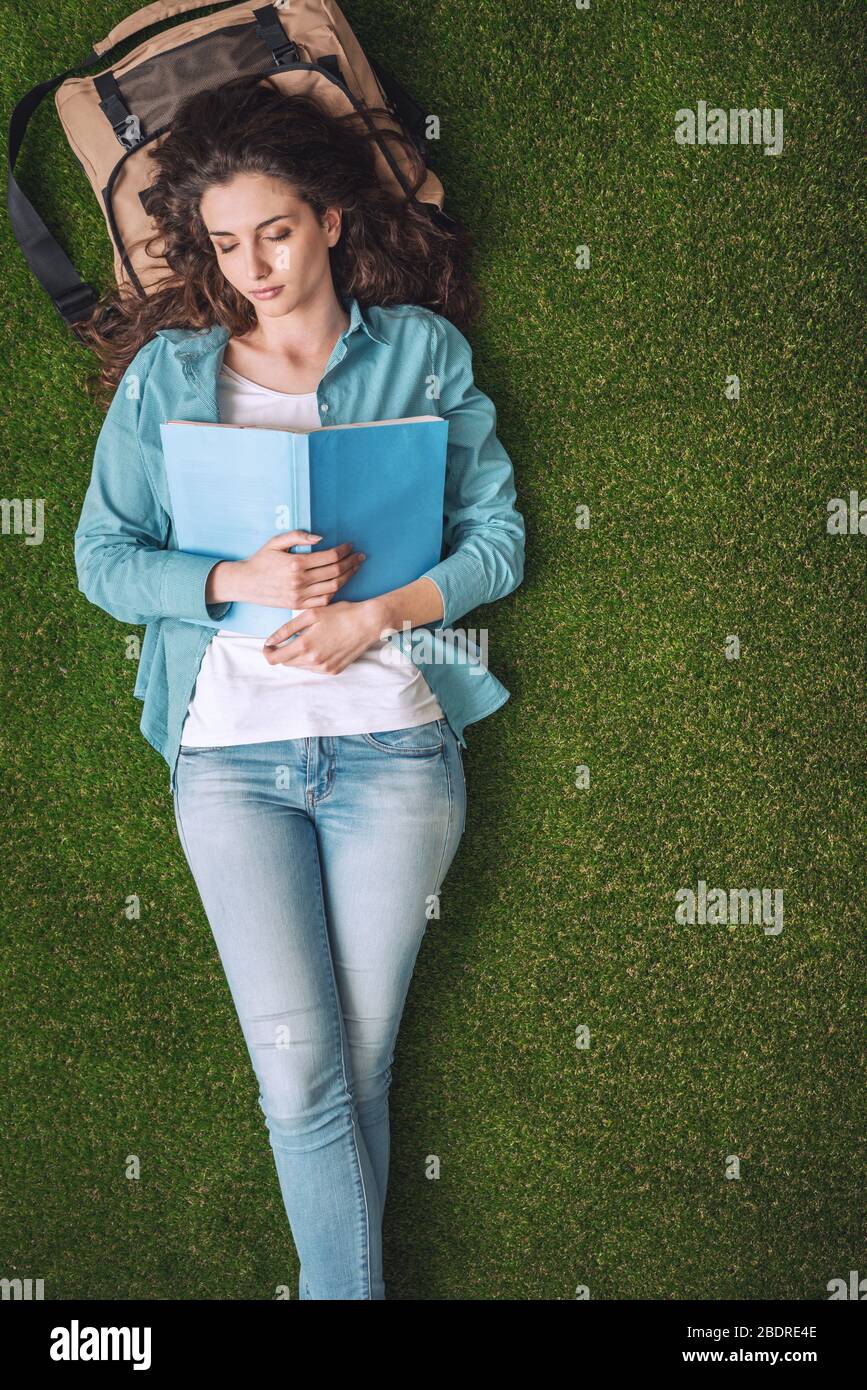 Belle étudiante en femme se relaxant dehors sur l'herbe, elle dort et tient un livre ouvert sur sa poitrine Banque D'Images