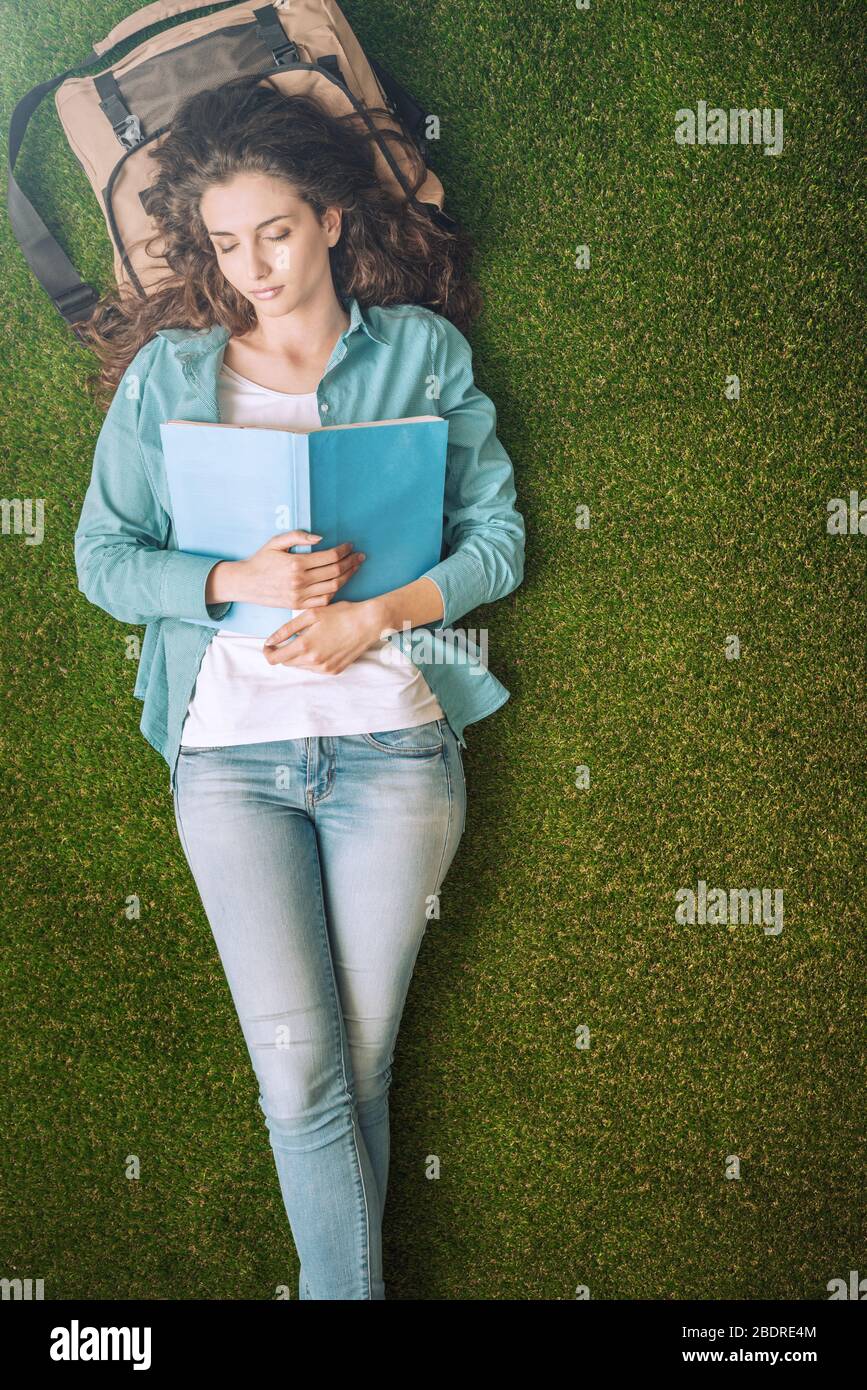 Belle étudiante en femme se relaxant dehors sur l'herbe, elle dort et tient un livre ouvert sur sa poitrine Banque D'Images