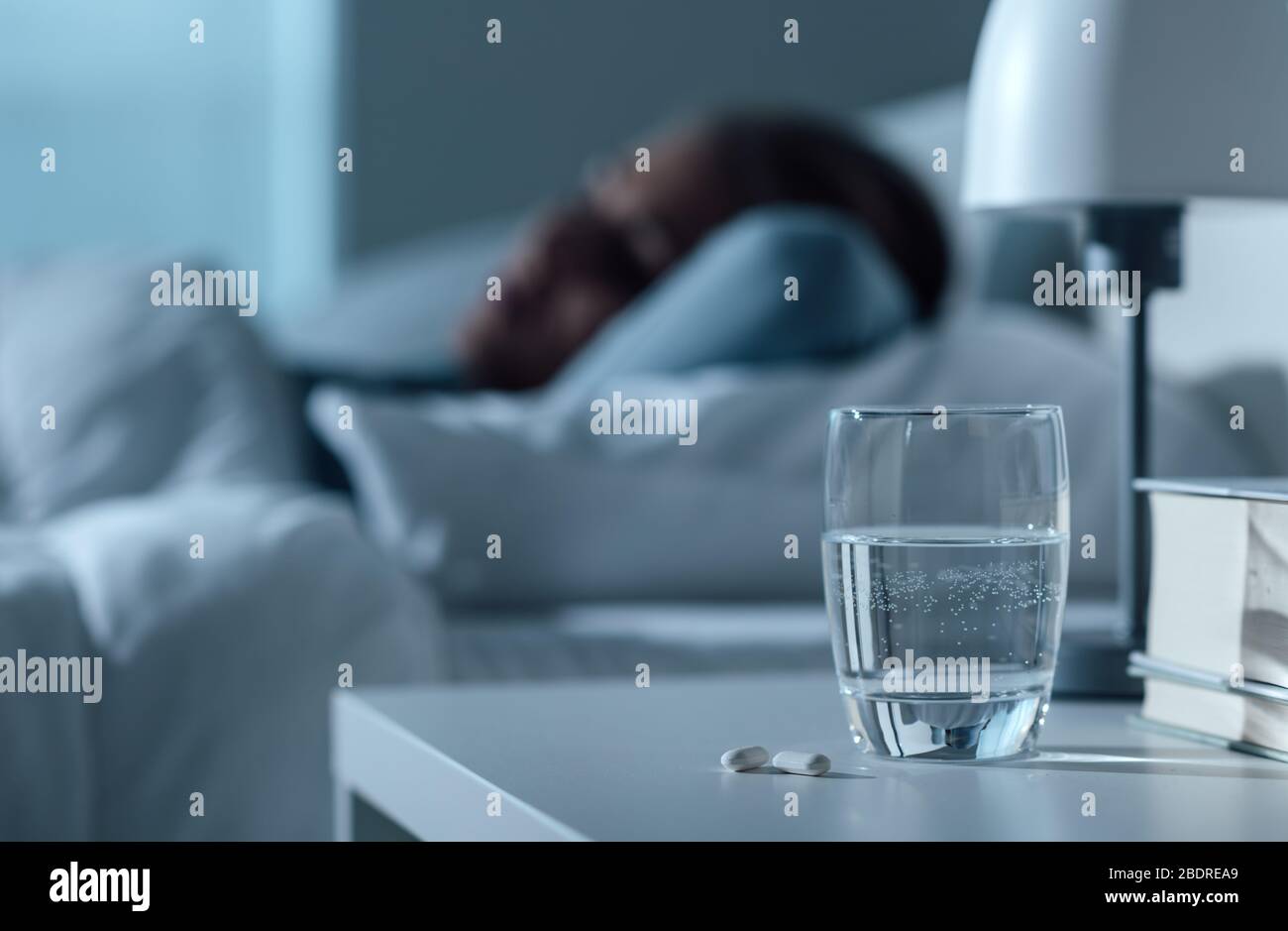 Femme dormant dans son lit la nuit, verre sur l'eau et pilules au premier plan, médecine et concept de traitement Banque D'Images