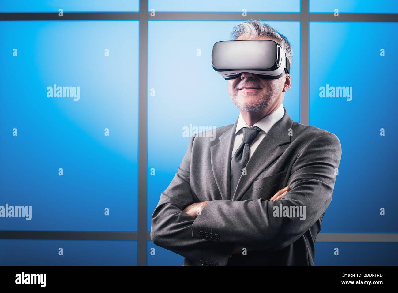Homme d'affaires éprouvé et confiant, confronté à une réalité virtuelle, il porte un casque VR et souriant Banque D'Images