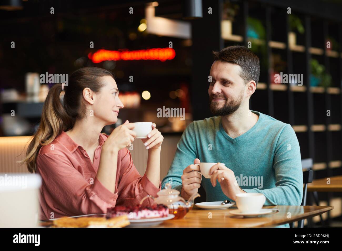 Jeune couple assis à la table avec une tasse de thé et parler les uns aux autres pendant leur date dans le café Banque D'Images