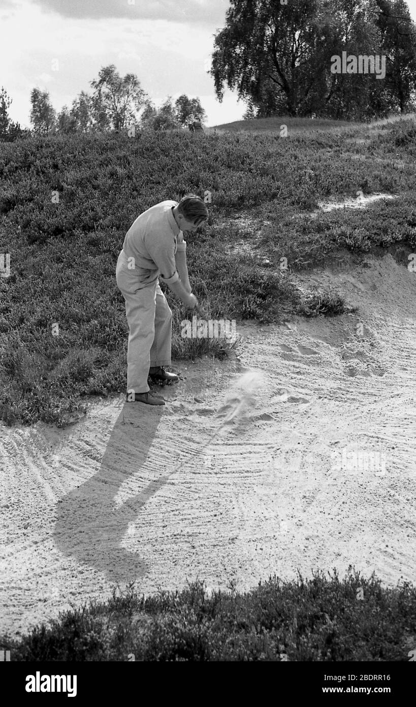 Années 60, golfeur jouant à partir d'un bunker vallonné sur terrain accidenté, Angleterre, Royaume-Uni. les bunkers sont des dangers ou des pièges sur un parcours de golf rempli de sable et sont placés sur un parcours de golf dans des positions stratégiques pour attraper des coups de feu et pénaliser un joueur. Banque D'Images