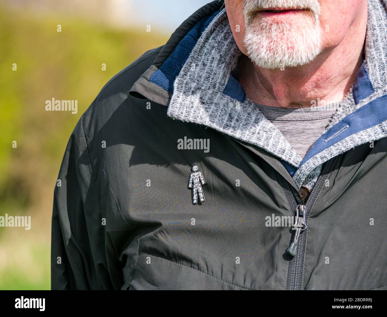 Homme senior avec barbe grise portant un badge caritatif Prostate Cancer UK épinglé à la veste pour sensibiliser le public à l'état de santé commun, Royaume-Uni Banque D'Images