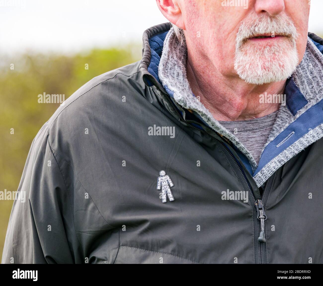Homme senior avec barbe grise portant un badge caritatif Prostate Cancer UK épinglé à la veste pour sensibiliser le public à l'état de santé commun, Royaume-Uni Banque D'Images