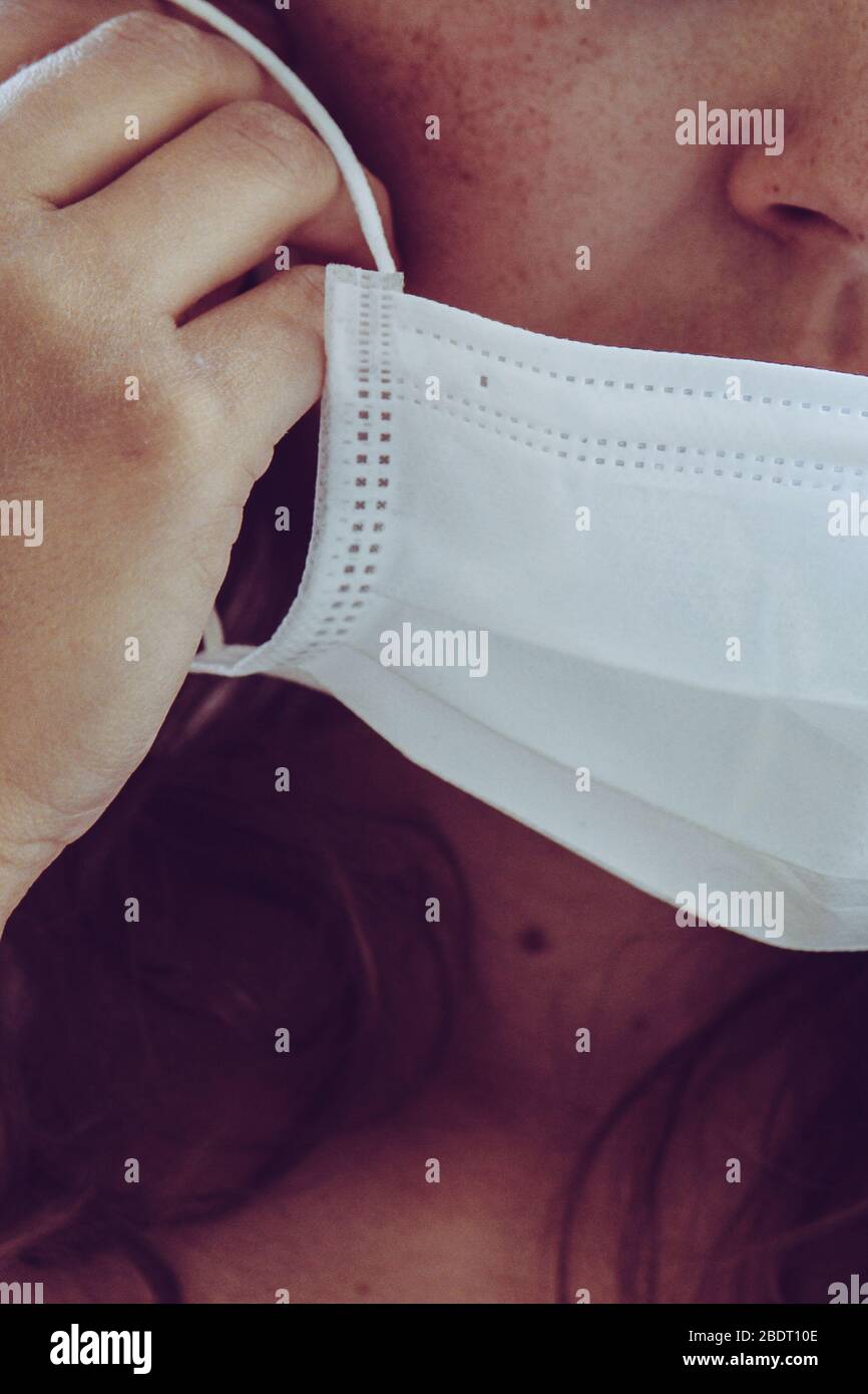 Détail du visage de femme non reconnaissable portant un masque médical blanc. Partiellement flou, mise au point sélective, grain léger. Fille REDEHEAD avec des taches. Coronavirus, COVID-19 quarantaine. Médecins, concept infirmière. Banque D'Images