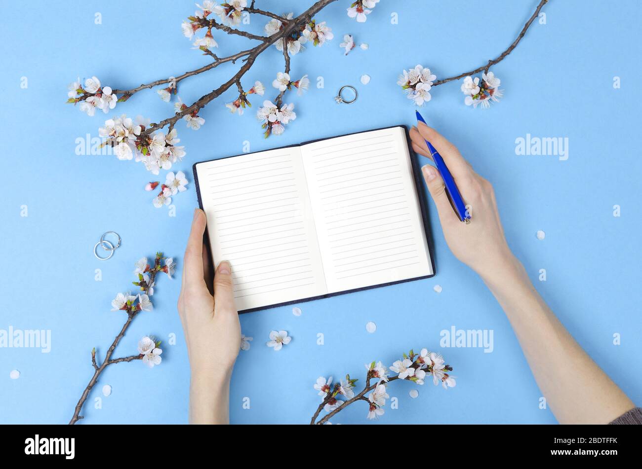 Fille écrivant la liste de souhaits pour les plans futurs. composition de plat avec fleurs, bloc-notes. Planification de mariage Banque D'Images