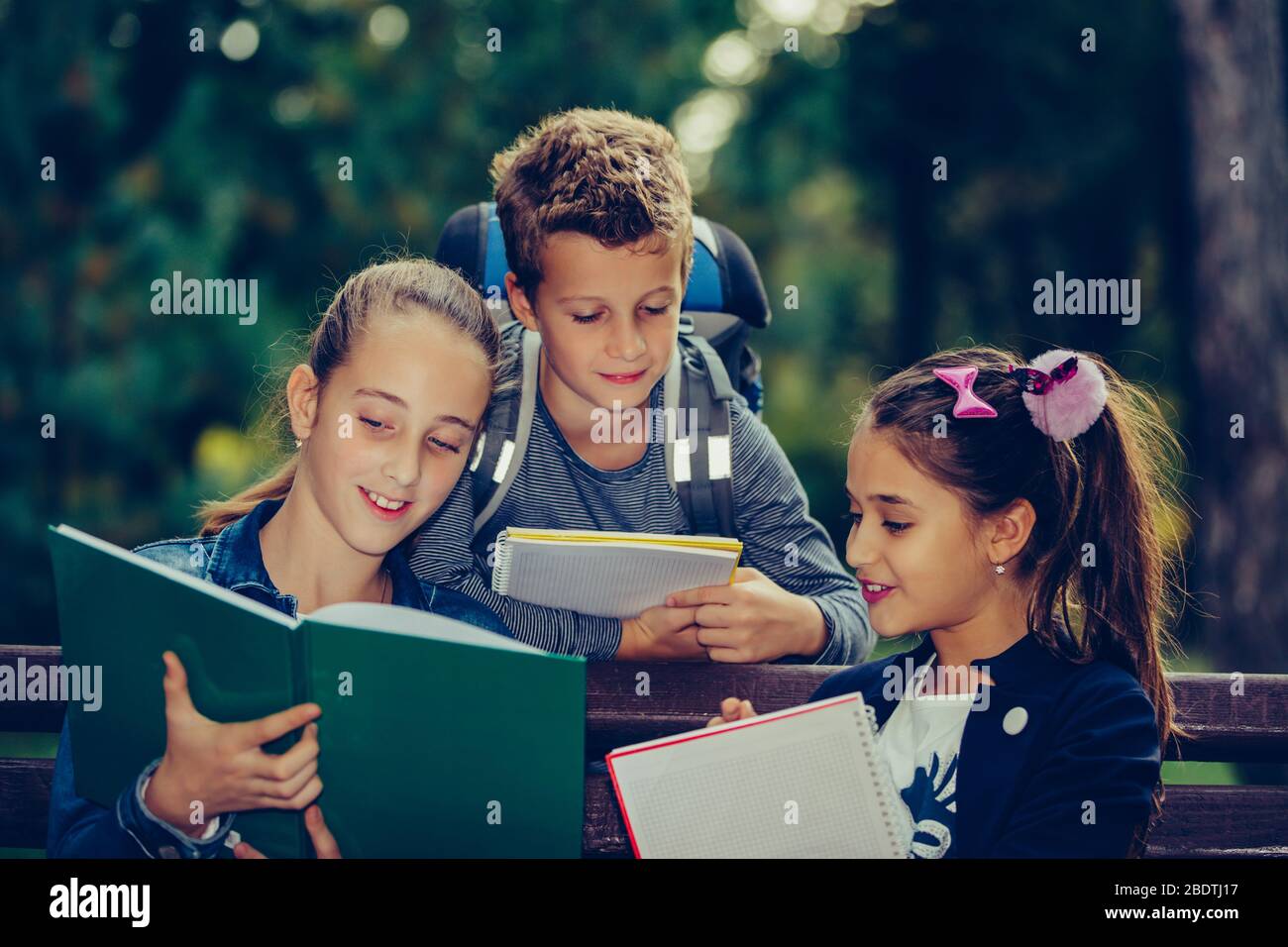 Retour à l'école. Les enfants avec des sacs à dos ont du plaisir, de parler, de lire un livre.Groupe d'écoliers élémentaires ayant une discussion sur les devoirs pendant leur déplacement Banque D'Images