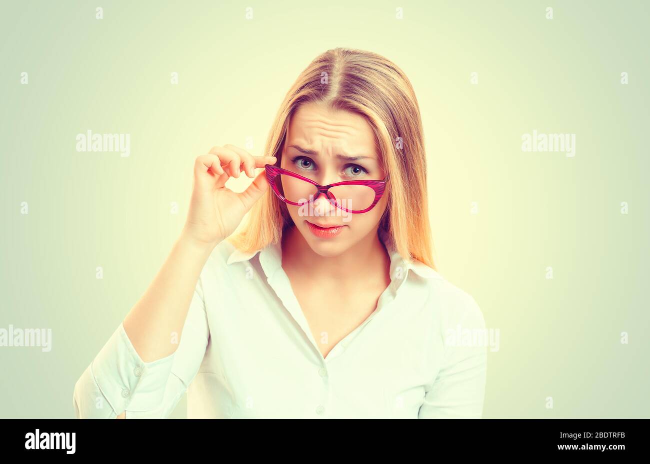 Headshot sérieuse femme sorceuse en colère tenant des lunettes de soleil vers le bas sceptique regardant vous isolé vert jaune mur fond, chemise blanche. Humain Banque D'Images