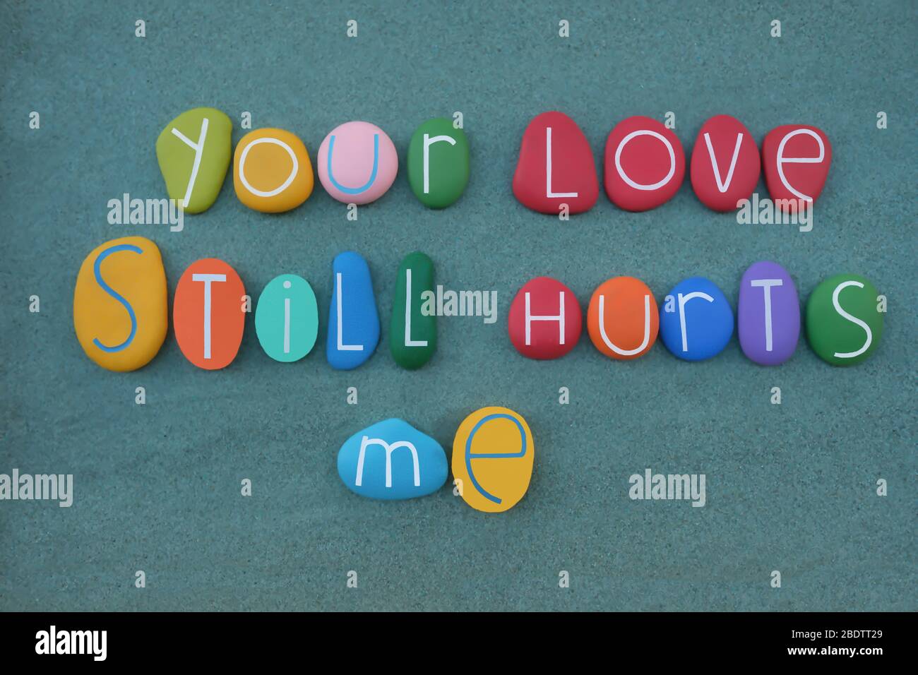 Votre amour me fait toujours mal, phrase composée de lettres de pierre multicolores sur le sable vert Banque D'Images