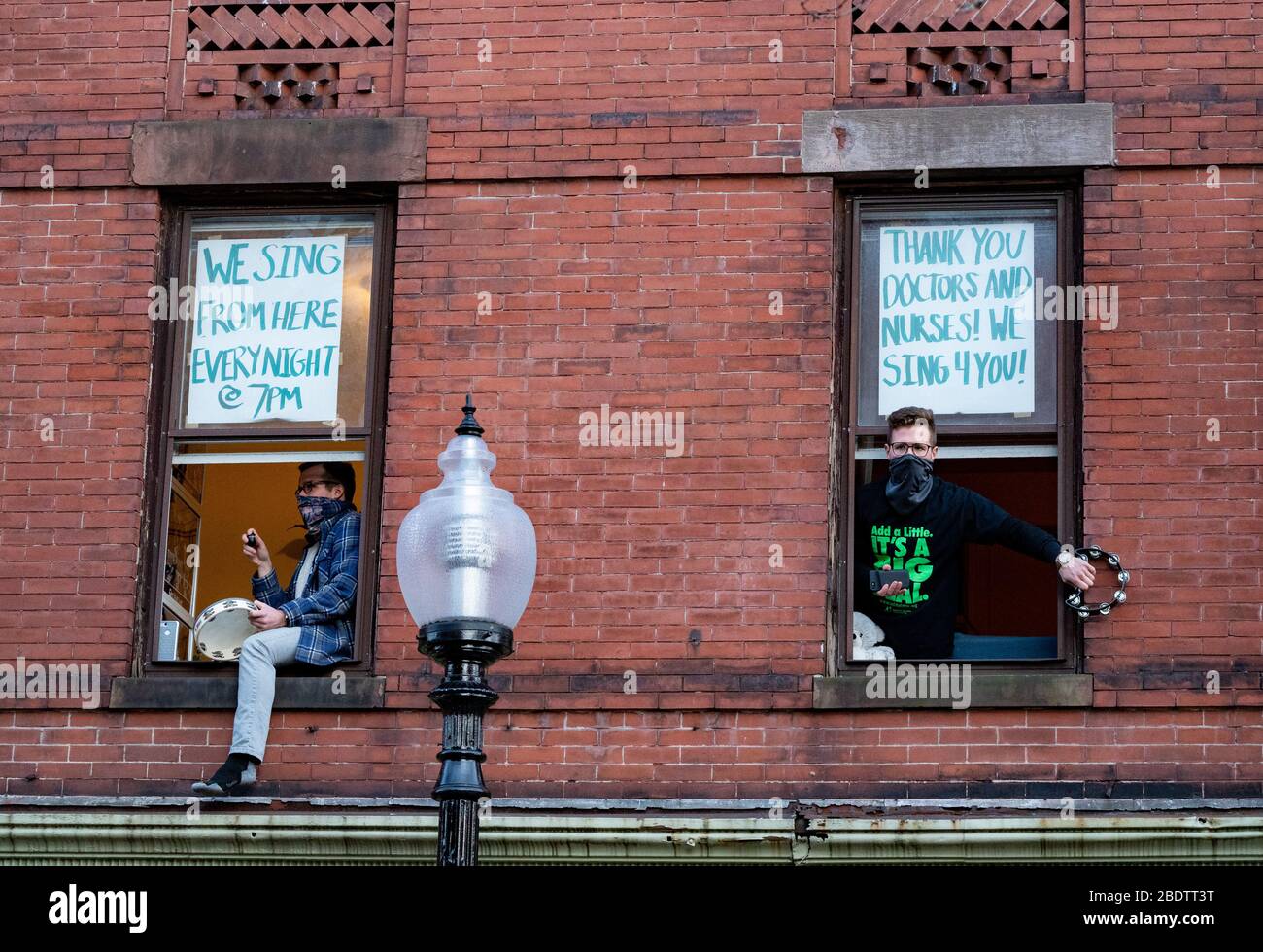 8 avril 2020, Boston, Massachusetts, États-Unis: Andrew Johnston (L) et Jessie Stettin jouant de la musique à partir de leur appartement au 2ème étage à Boston. Le duo joue de la musique de sa fenêtre à 19 h 30 minutes pour ceux qui aiment écouter avec eux, tout en suivant les directives de distanciation sociale. Banque D'Images