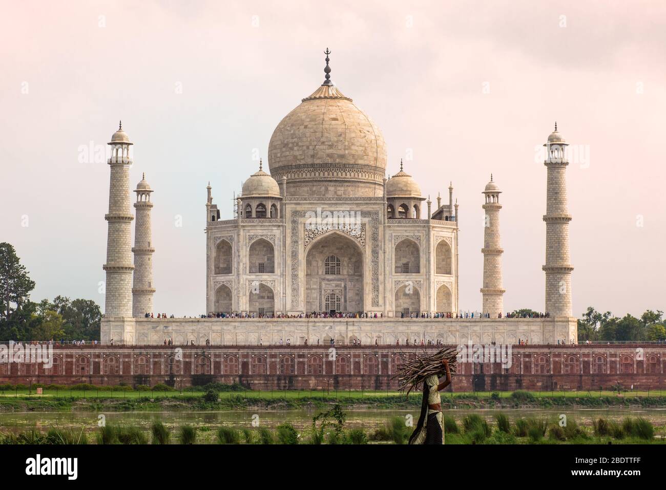 Taj Mahal au coucher du soleil avec une femme locale transportant du bois au premier plan. Banque D'Images