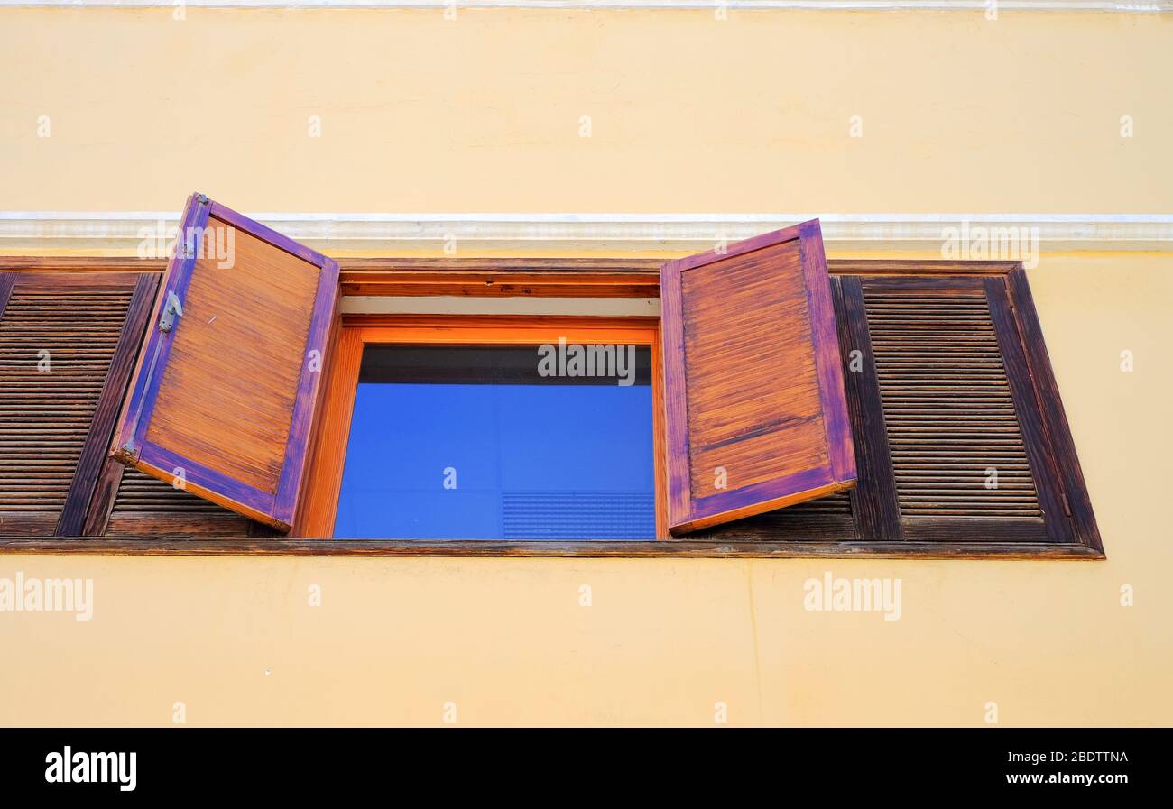 Fenêtre reflétant le ciel bleu, volets en bois ouverts larges, mur, vue de bas angle. Banque D'Images