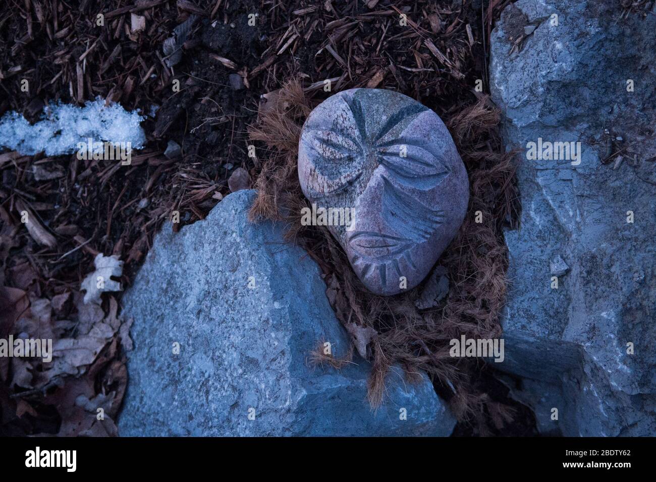 Masque visage sculpté dans la pierre avec des feuilles de cheveux regardant comme portrait femelle de Rock et des feuilles et des brindilles de neige signifiant Thaw de printemps Banque D'Images