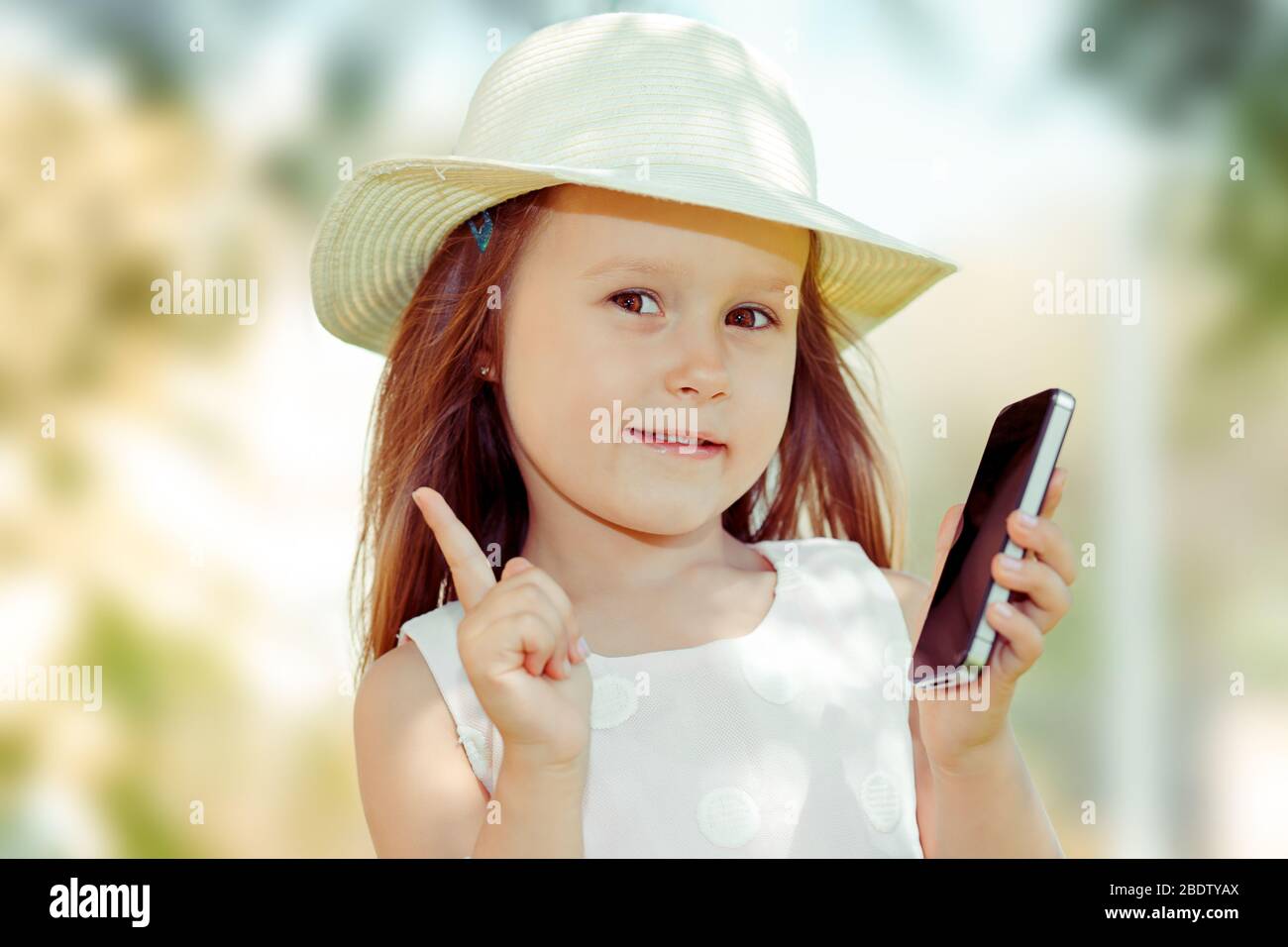 Enfant avec smartphone. Gros plan portrait de jolie fille enfant tenant le téléphone cellulaire montrant non, ne pas, attention avec le doigt de geste de main. Blocage dangereux Banque D'Images