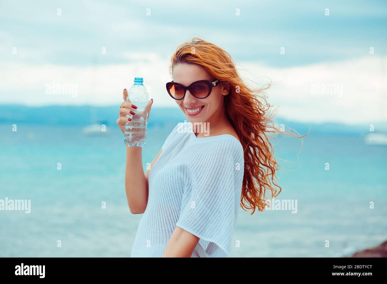Belle jeune femme brunette dans des lunettes de soleil buvant de l'eau et  se refroidissant après avoir courir à la plage sur un fond de mer. Effet de  filtre Instagram ap Photo
